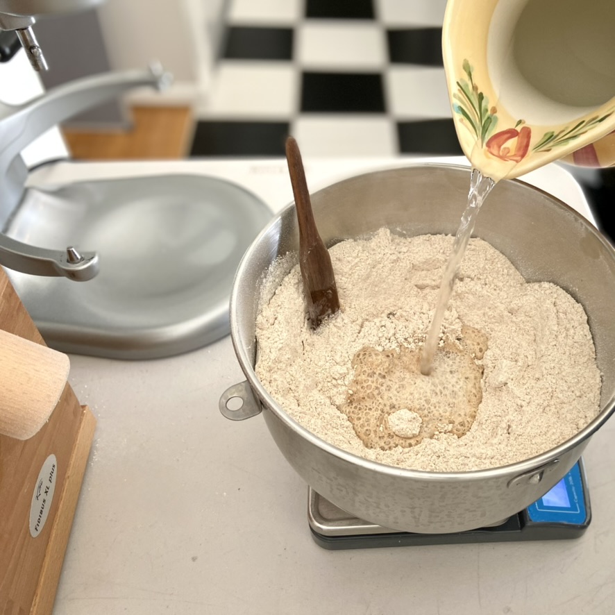 Someone weighing water directly into a mixing bowl sitting on a kitchens scale