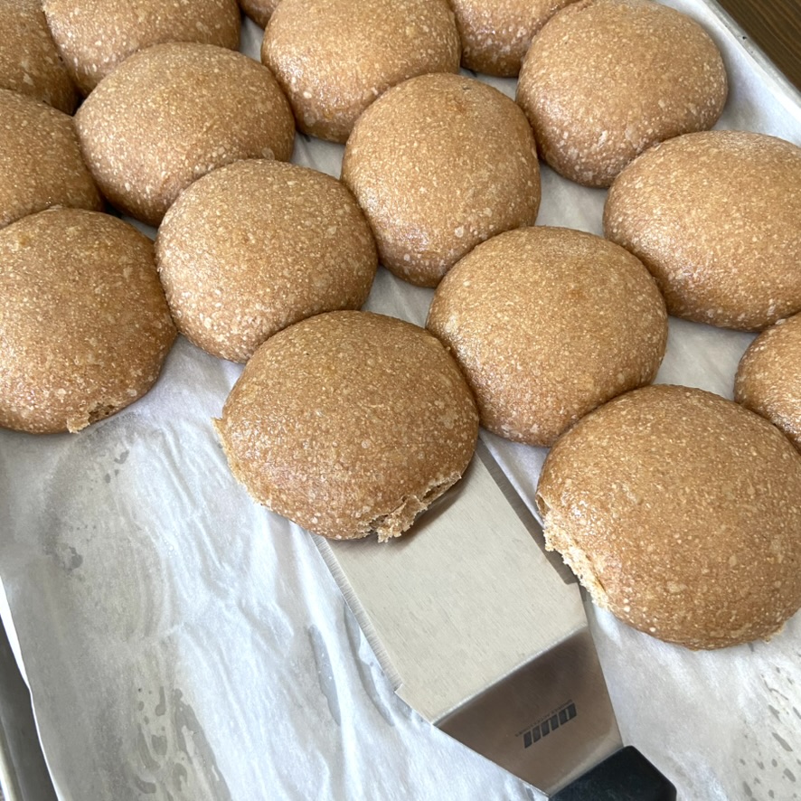 Sourdough buns sitting on a pan with someone using a spatula to pick one up