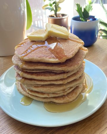 Stack of pancakes on a plate with butter and maple syrup on top