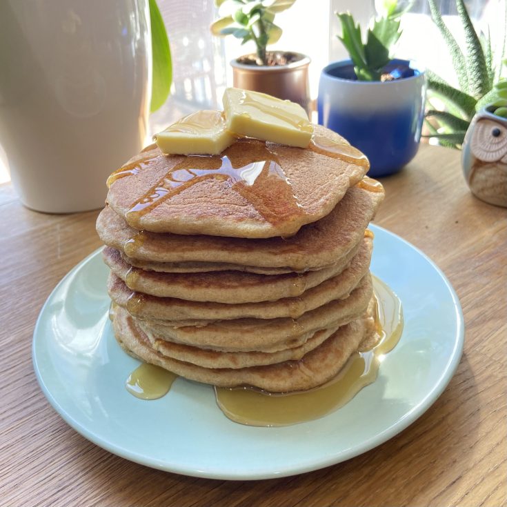Stack of pancakes on a plate with butter and maple syrup on top