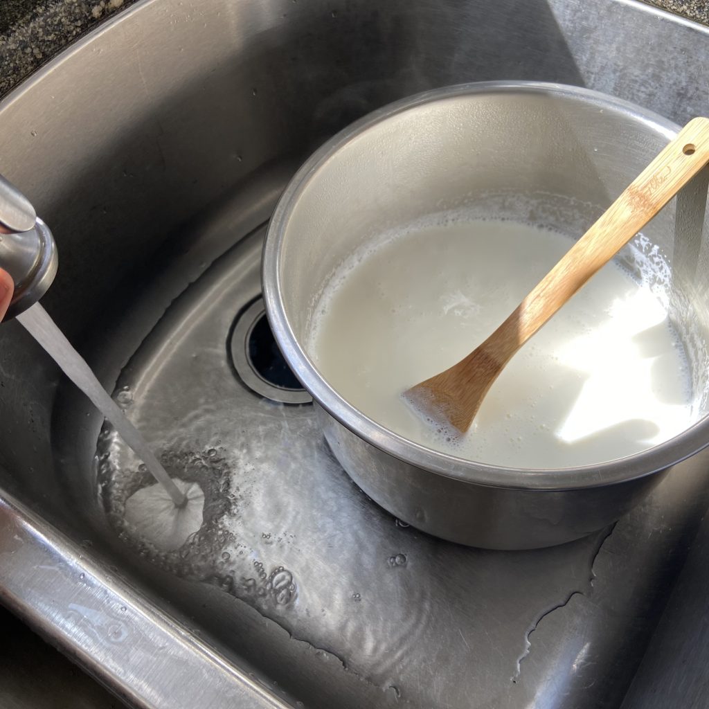 Pot of hot milk resting in a sink that is being filled up with cold water