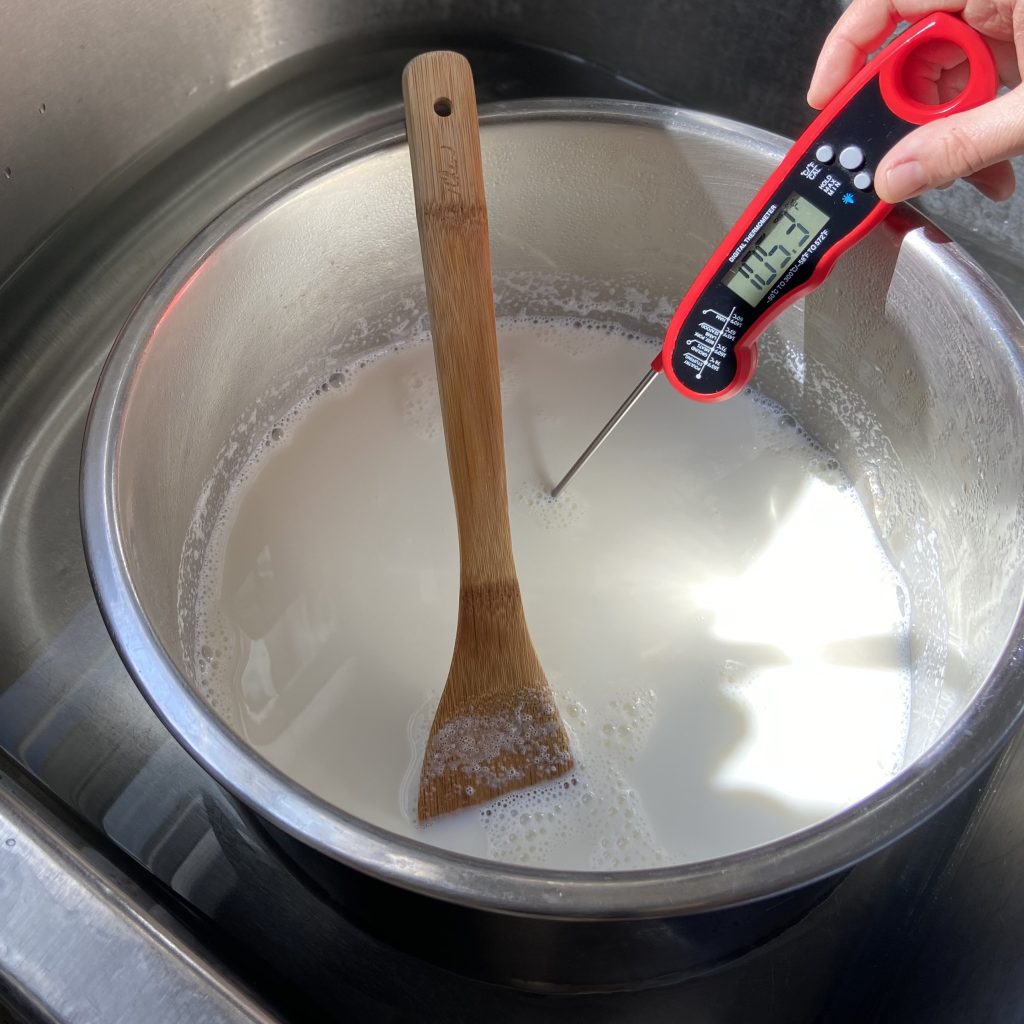 A pot of milk in the sink, someone taking its temperature with a meat thermometer