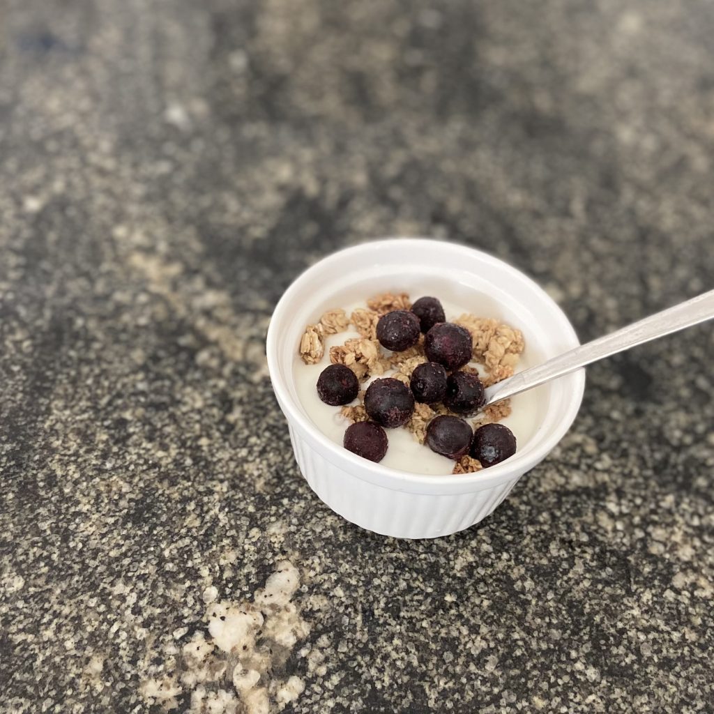 Yogurt in a bowl topped with granola and frozen blueberries