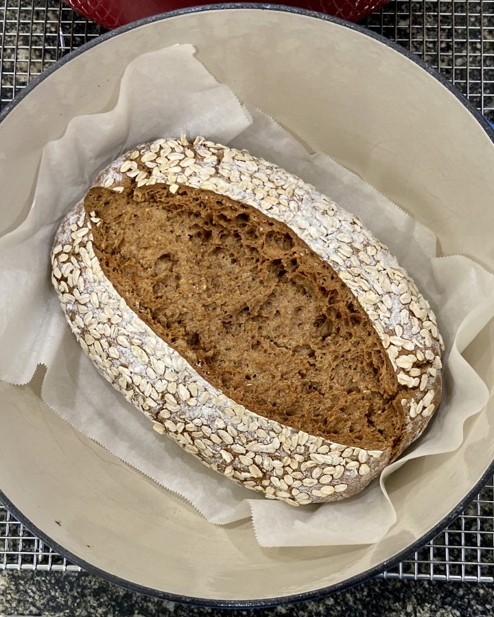 A loaf of baked oatmeal rye sourdough bread resting in a dutch oven just after it was removed from the oven.