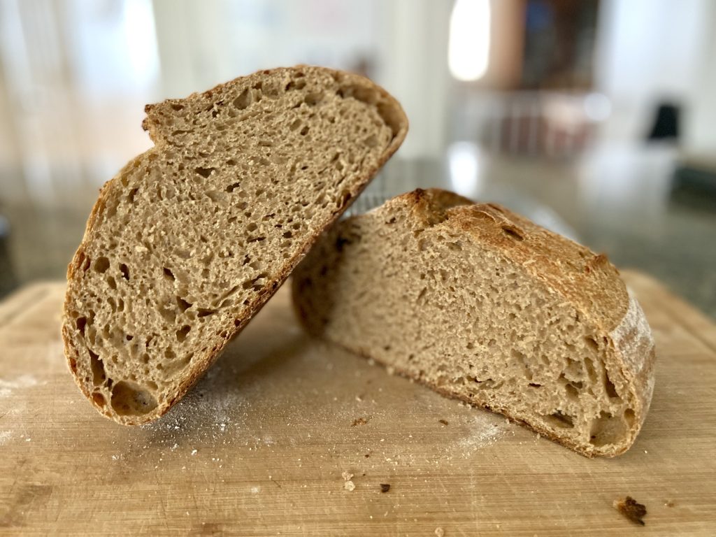 A loaf of sourdough bread cut in half and resting on a cutting board to display the crumb of the bread.
