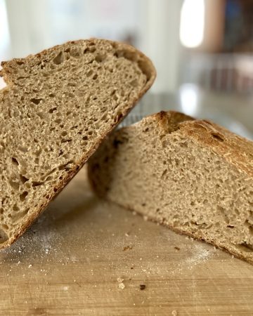 A loaf of sourdough bread cut in half and resting on a cutting board to display the crumb of the bread.